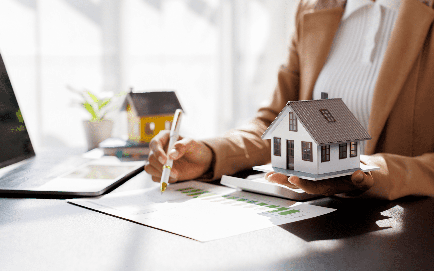Person holding model house, signing real estate documents